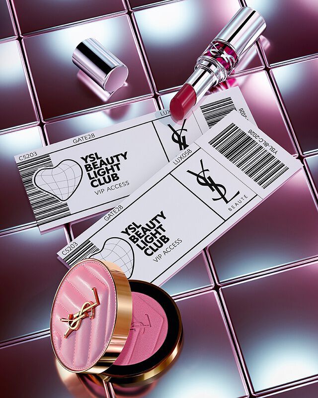 Rouge a levres Loveshine teinte Make Me Blush et deux invitations VIP YSL Beauty Light Club sur un fond en carrelage reflechissant.