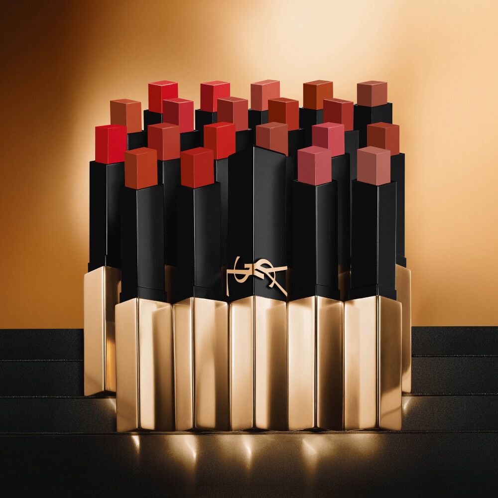 Meerdere smalle vierkante lipsticks van Yves Saint Laurent in verschillende rood- en nudetinten op een gouden achtergrond.