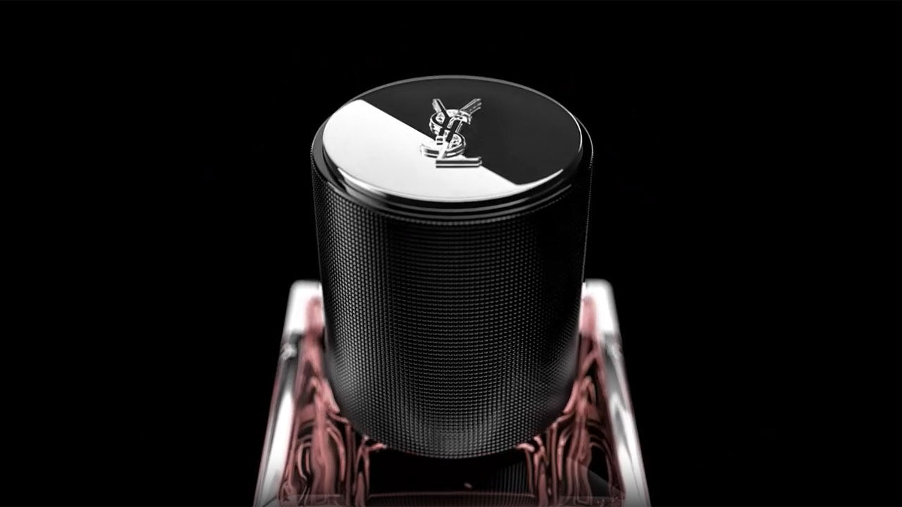 A close-up of a sleek, metallic cylindrical bottle with a reflective cap featuring a logo, set against a black background with subtle pink accents.