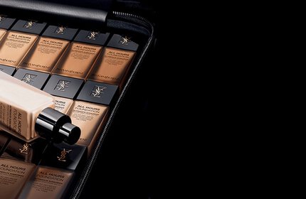 A collection of foundation bottles arranged neatly inside a black case, showcasing various shades of the product. The scene has a sleek, modern aesthetic with a dark background.