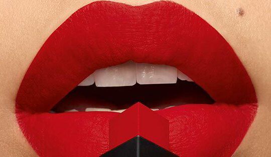 Close-up of a pair of lips painted bright red, with a stark contrast to white teeth, and a black and red lipstick bullet positioned centrally below the mouth.