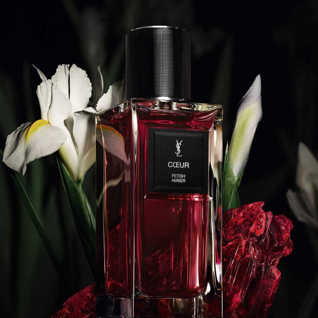 Flacon de parfum YSL rouge avec des fleurs d’iris blanches sur fond sombre.