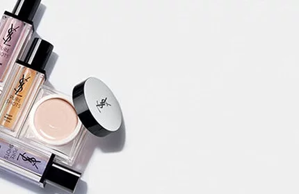 A collection of various makeup products arranged neatly, including foundations, concealers, and primers, against a white background.