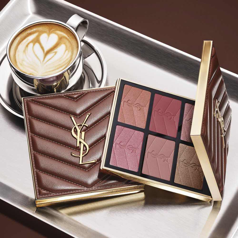 Palette de maquillage YSL et pochette matelassee a cote d’un cafe sur un plateau argente.