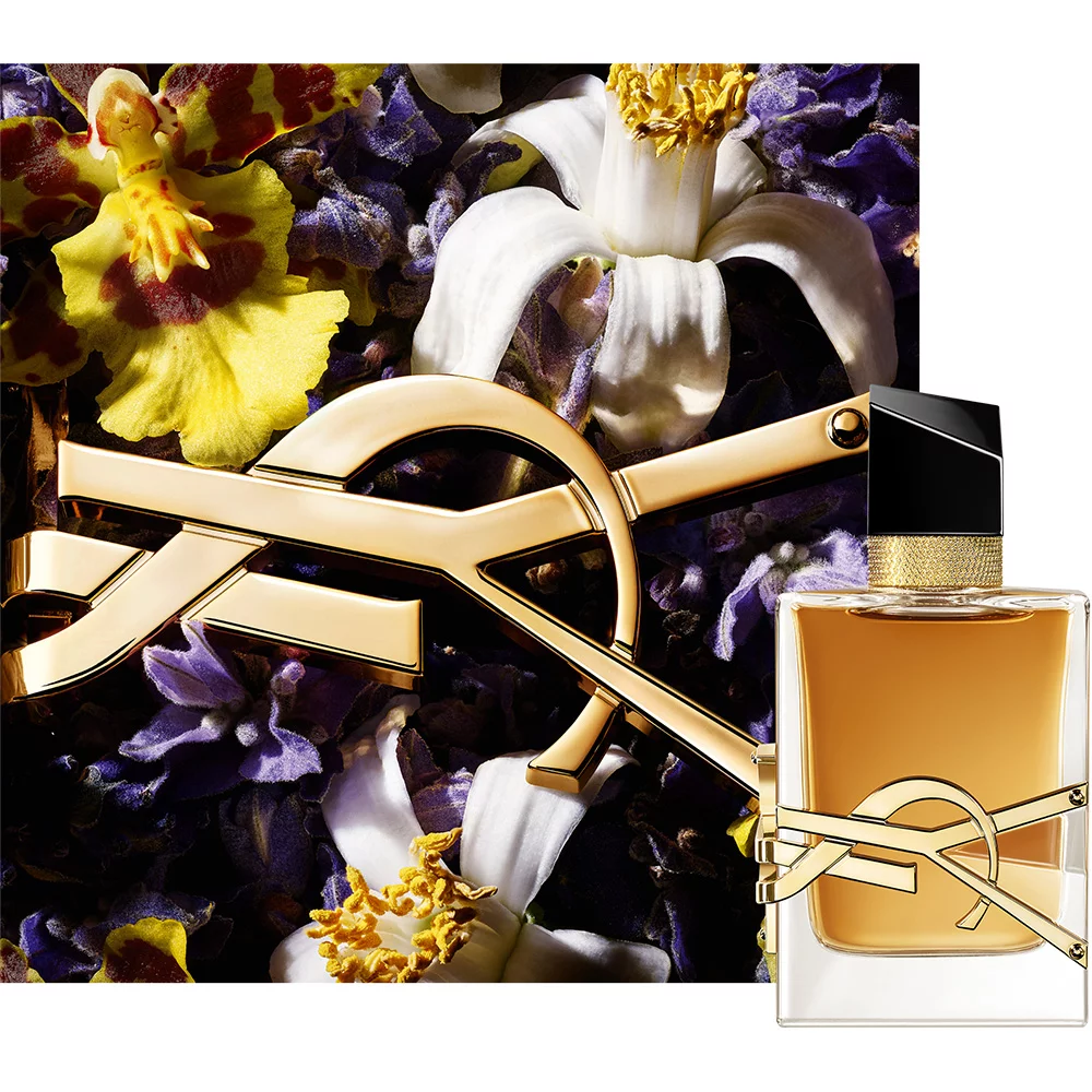 A perfume bottle with a sleek design featuring a golden cap and label, placed against a floral background with purple and yellow orchids.