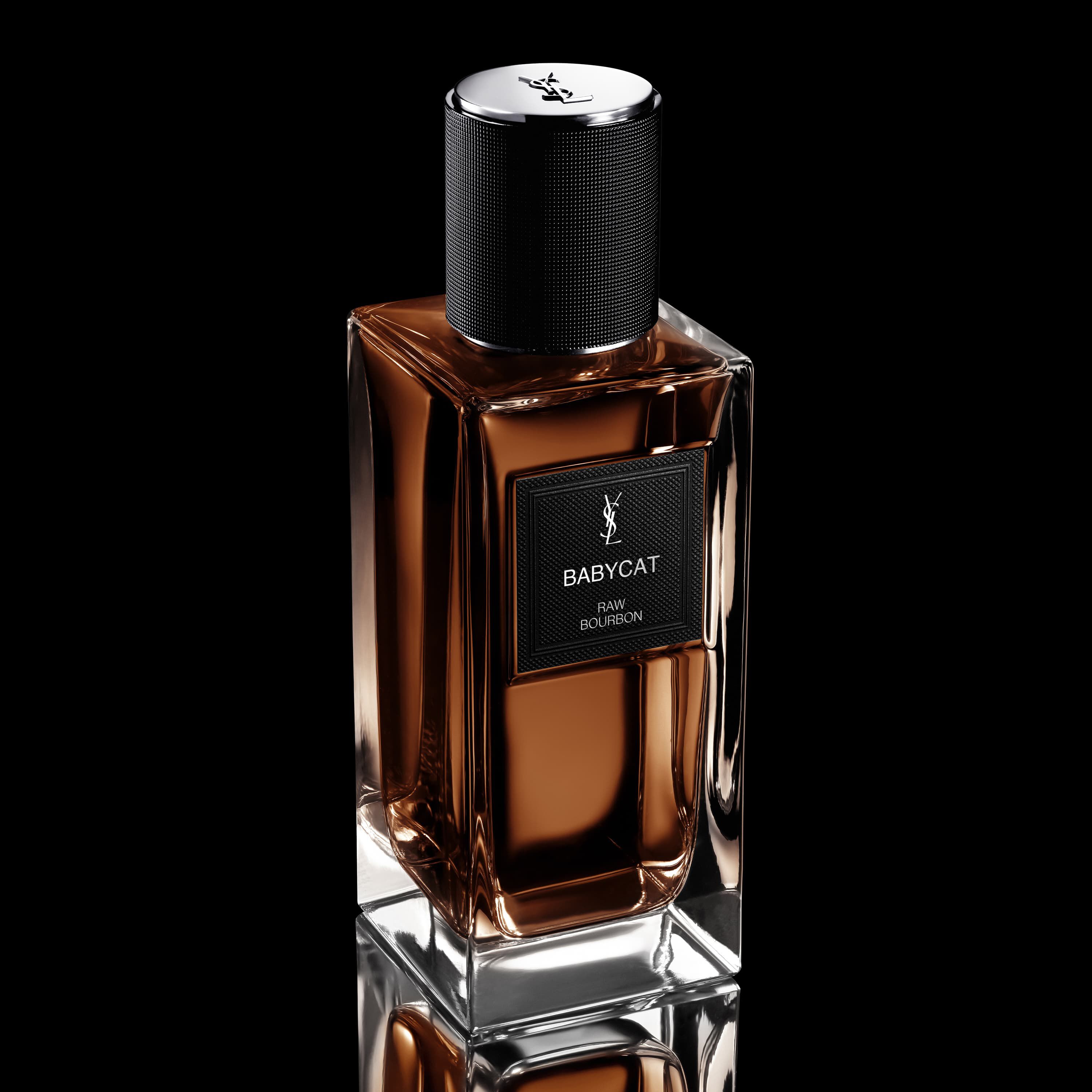 Flacon de parfum YSL Babycat Raw Bourbon avec liquide brun, etiquette noire et bouchon noir texture.