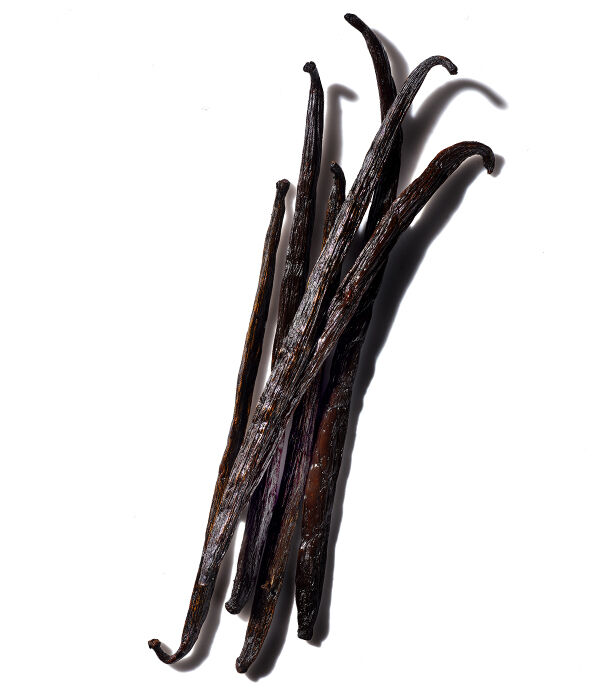A group of five dark brown vanilla bean pods arranged on a white background.