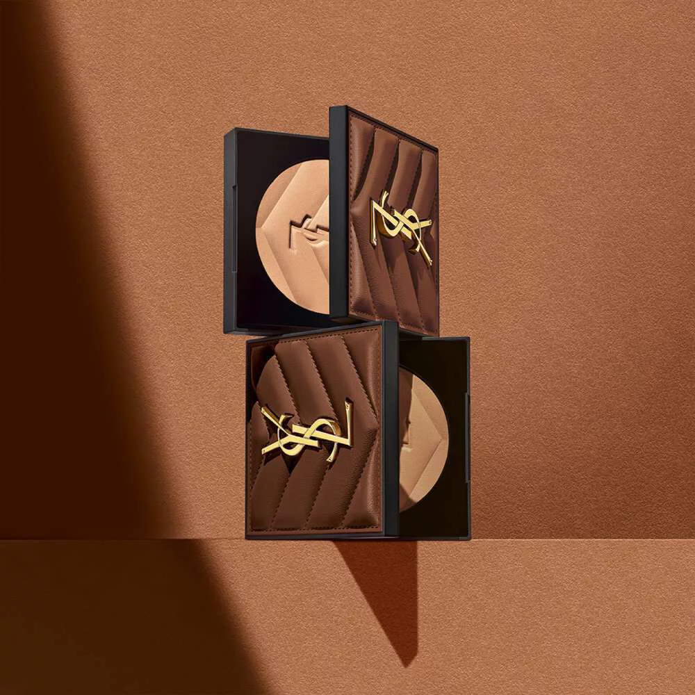 Three elegant makeup compacts with a quilted design and a gold logo, arranged against a warm brown background.