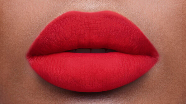 Close-up of vibrant red lips with a smooth matte finish against a warm skin tone backdrop.