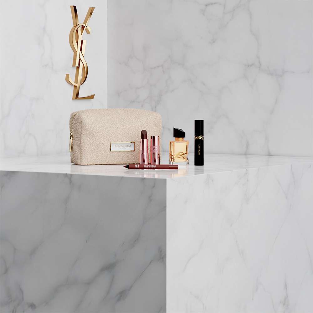 Trousse, parfum Libre et maquillage YSL sur fond marbre blanc.