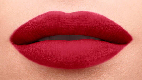 Close-up of full lips painted in a deep red matte lipstick, with a smooth and defined shape.
