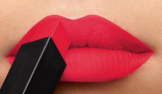 A close-up of vibrant red lips with a bullet lipstick being applied. The lipstick case is black.