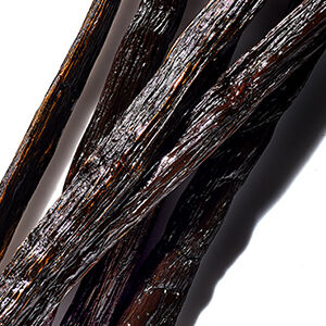 Close-up view of dark, shiny vanilla bean pods, showcasing their textured surfaces and deep brown hues against a white background.