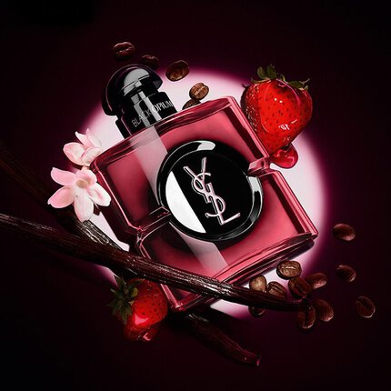 Flacon de parfum YSL Black Opium entoure de grains de cafe, de fraises, de gousses de vanille et de fleurs blanches sur fond sombre.