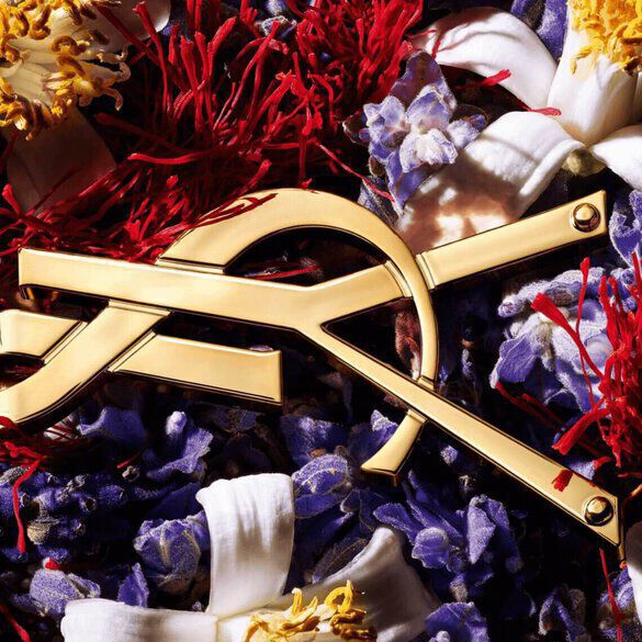 A golden compass laid over a colorful arrangement of flowers and red threads.