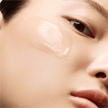 A close-up of a person's face showing a smooth, translucent skincare product applied to the cheek. The skin appears clean and glowing.