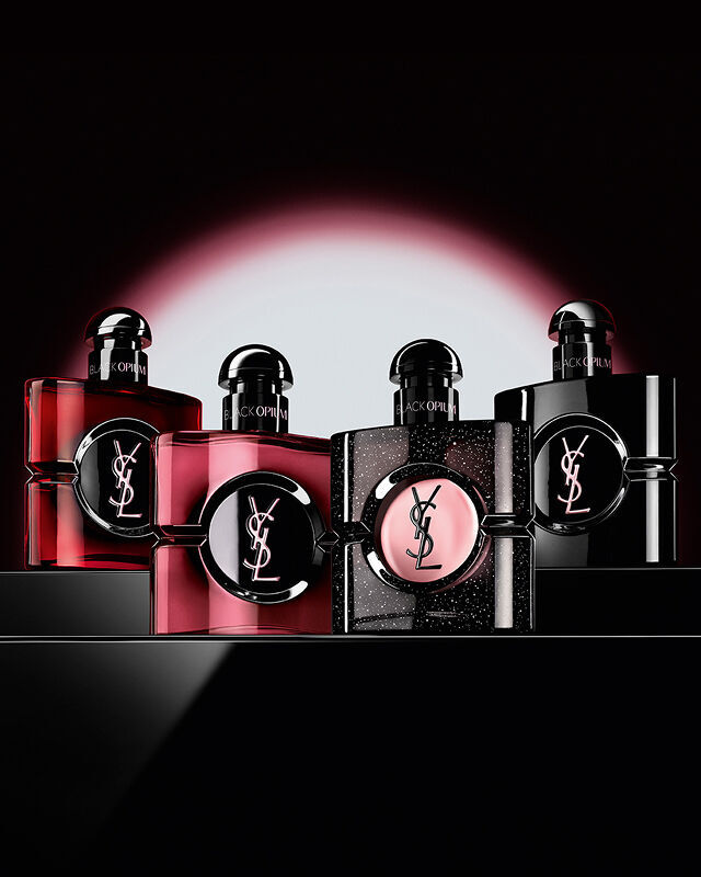Four different Black Opium perfume bottles displayed in a row on a dark, reflective surface.