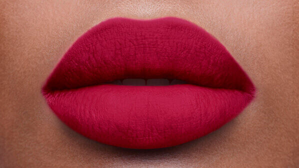 Close-up of a pair of full lips coated in a deep red matte lipstick against a neutral skin tone background.