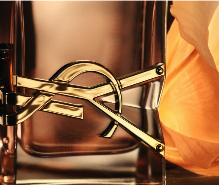 A close-up of a perfume bottle with a gold geometric design and a soft orange flower in the background, highlighting elegance and sophistication.