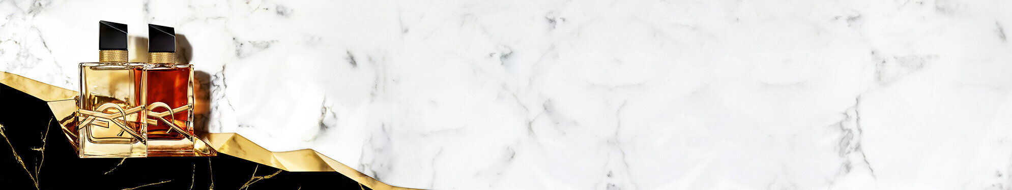Two elegant perfume bottles are positioned on a marble surface with a black and gold accent. The background features a sleek white marble texture.