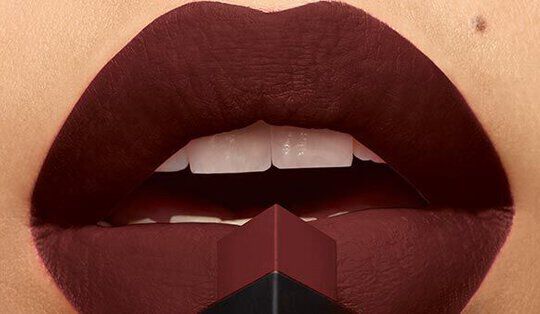 Close-up of elegantly shaped lips wearing deep burgundy lipstick, with a lipstick bullet positioned in front.