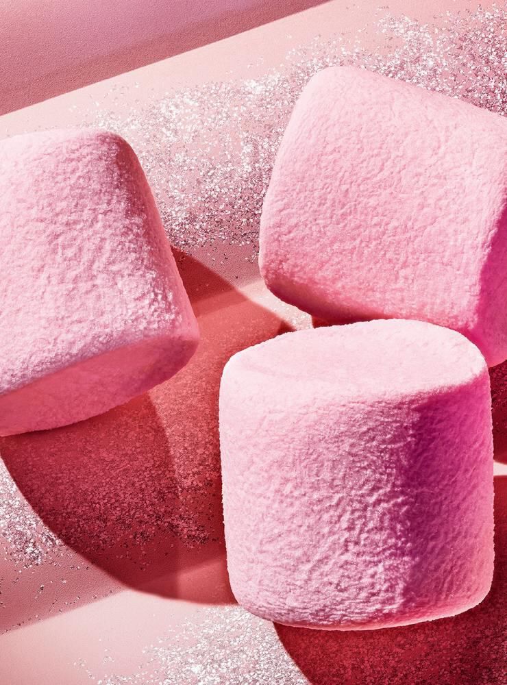 Three pink marshmallows on a glittery pink background.
