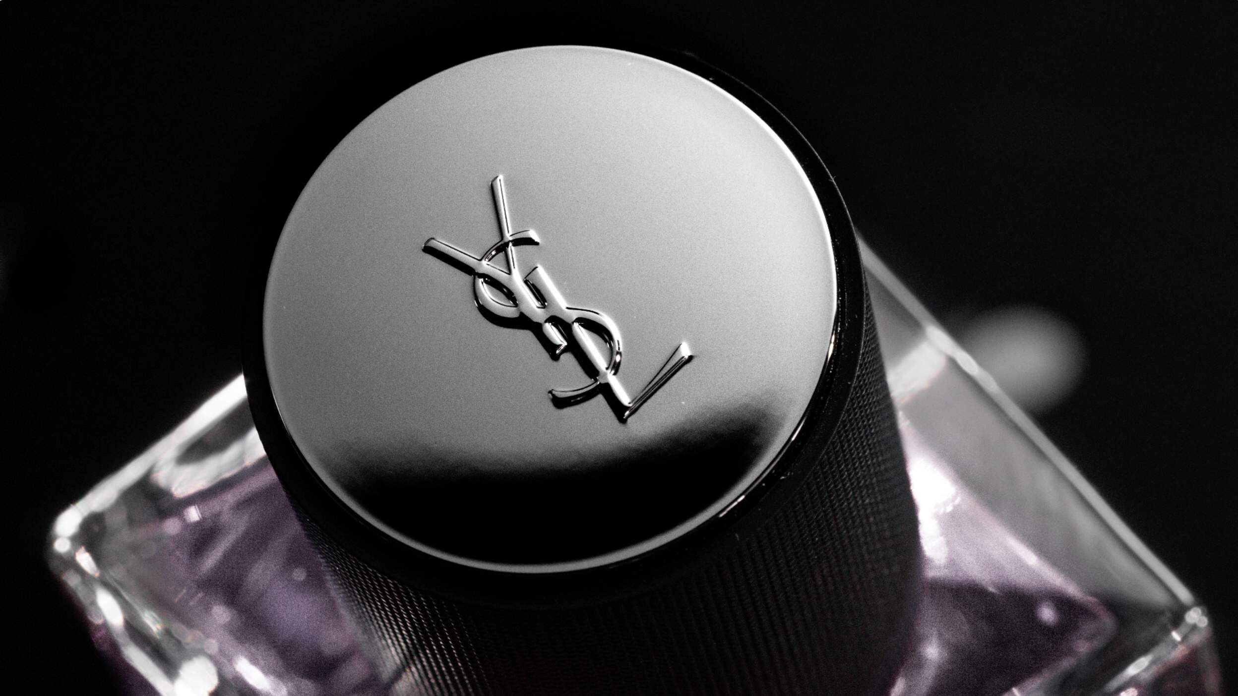 Close-up of a perfume bottle cap featuring the YSL logo, set against a black background.