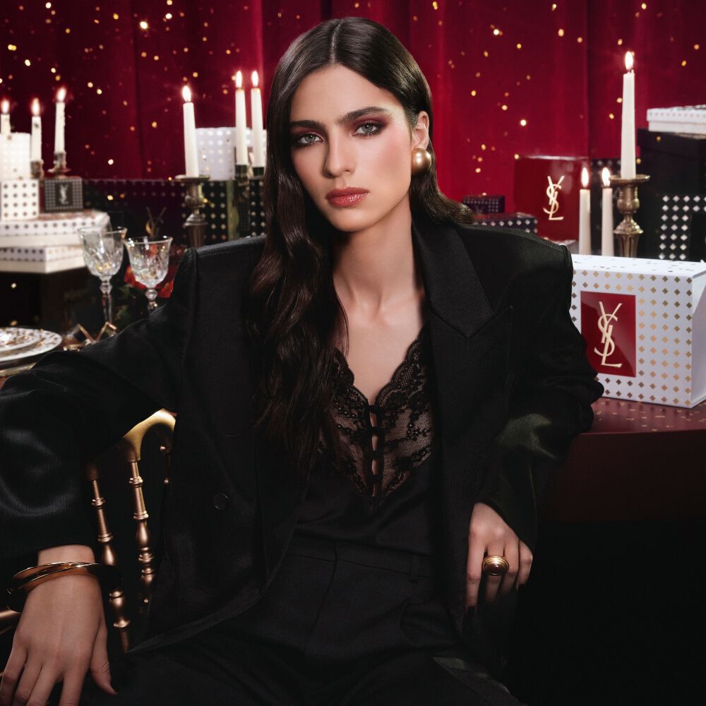 Model in een zwart pak en glamoureuze look, gezeten in een feestelijke kaarsverlichte setting met YSL cadeauverpakkingen. Model in een zwart pak en glamoureuze look, gezeten in een feestelijke kaarsverlichte setting met YSL cadeauverpakkingen. Model in een zwart pak en glamoureuze look, gezeten in een feestelijke kaarsverlichte setting met YSL cadeauverpakkingen.