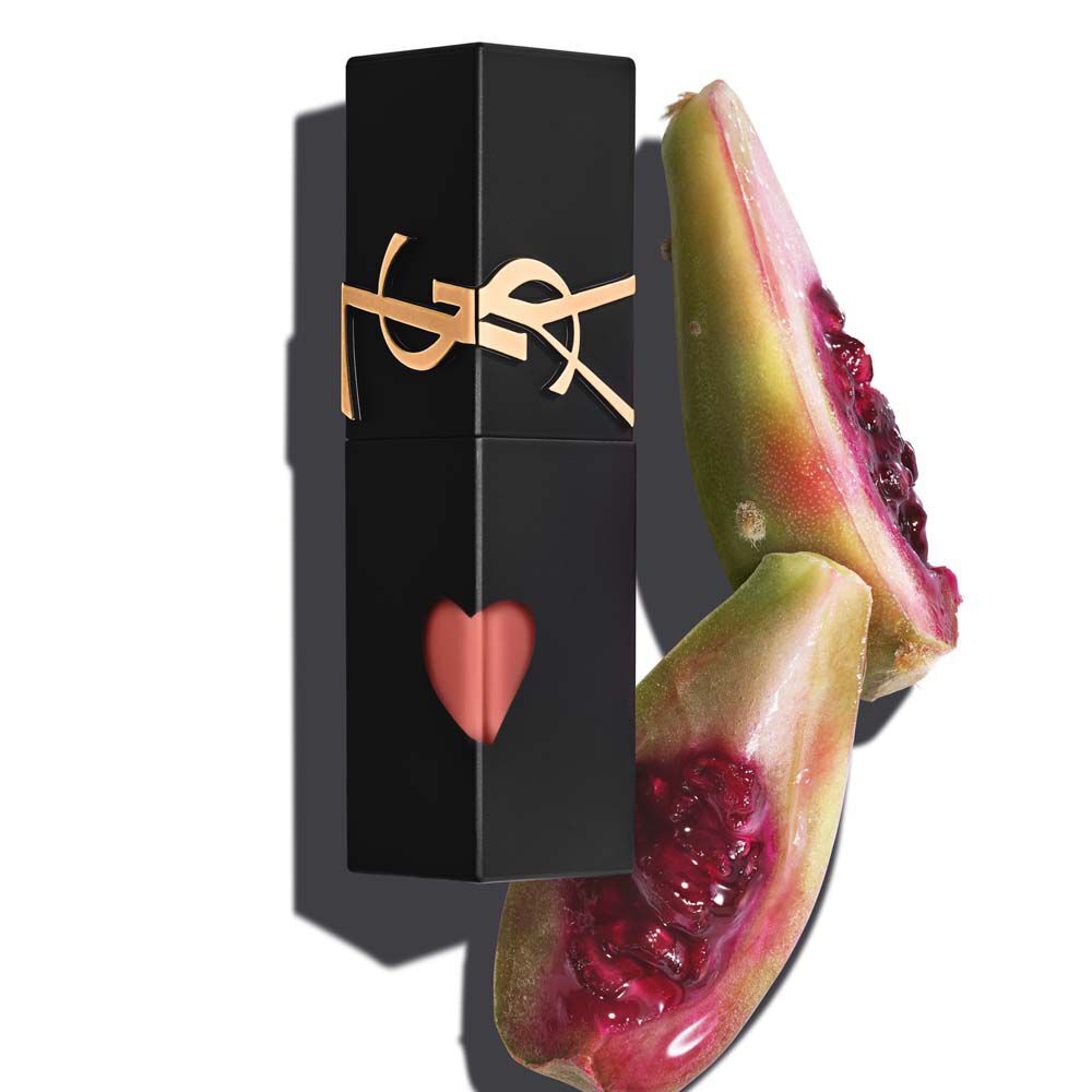 Un flacon de YSL THE INKS, teinture pour levres, decoupe d’un coeur, pose a cote de deux moities d’une figue de Barbarie rose, juteuse et mure a point.