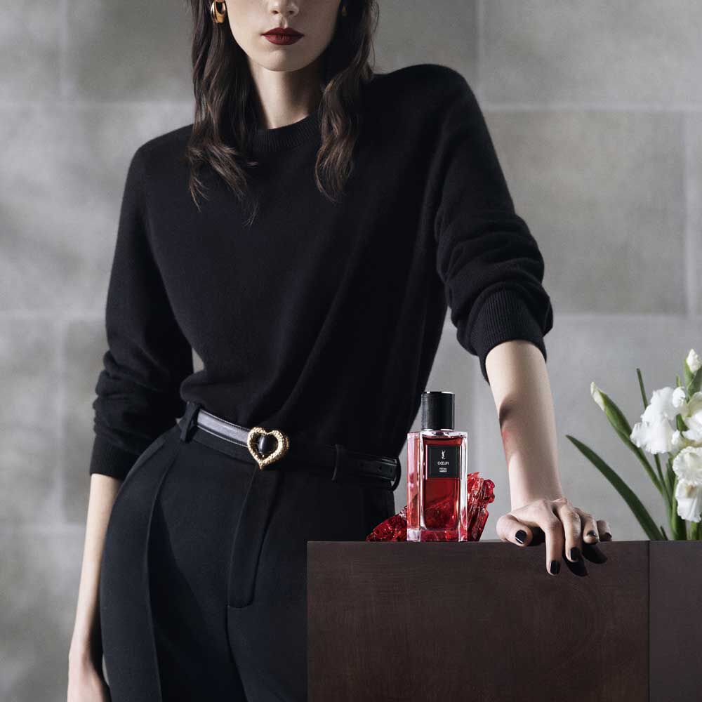 Een model is gekleed in het zwart, poserend naast de COEUR-parfumfles voor YSL Beauty.