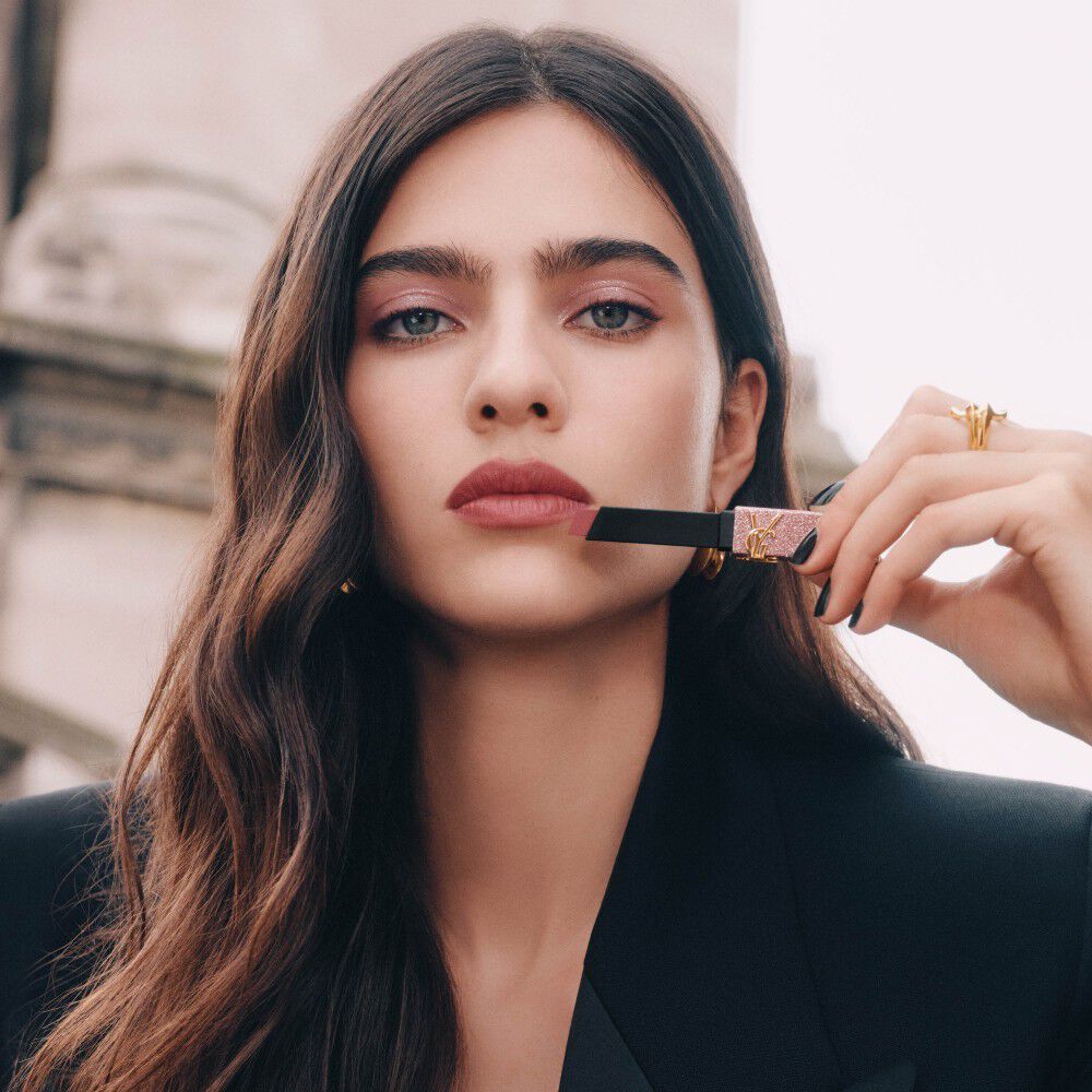 Model Loli Bahia holding YSL Rouge Pur Couture The Slim Lipstick in shade 835, applied on her lips, with a glitter case.