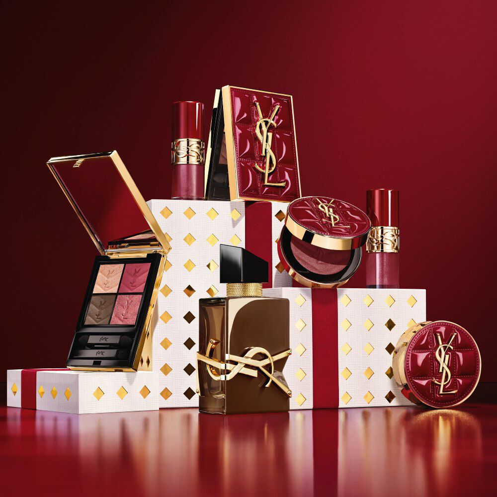 Collection maquillage et coffret parfum YSL Holiday 2026 poses sur des socles blancs a pois dores, dans un rouge bordeaux.