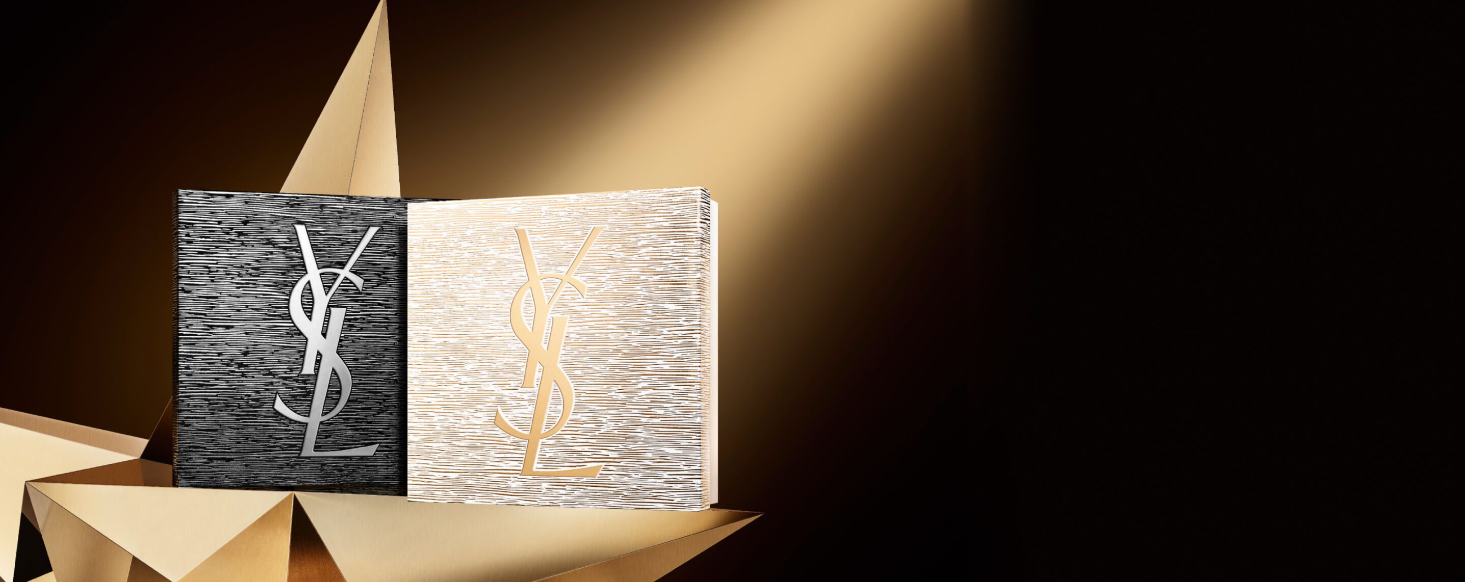 Deux élégants coffrets cadeaux de Noël YSL Beauté, l'un noir avec un logo argenté et l'autre doré avec un logo doré, placés sur une surface dorée géométrique, évoquant la couture et la brillance.