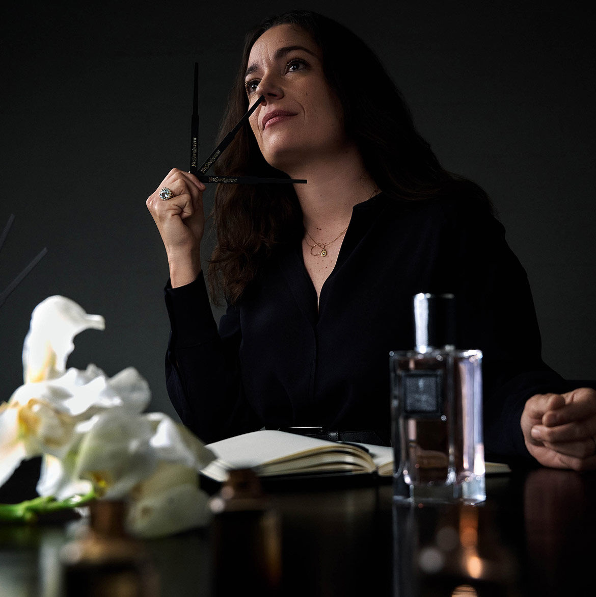 Femme sentant des mouillettes de parfum, avec carnet et flacon.