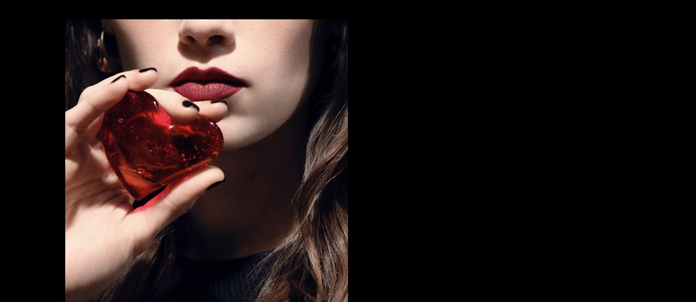 Close-up van de lippen en hand van een model
dat een doorschijnend robijnrood hartjuweel
vasthoudt voor YSL CŒUR Eau de Parfum.