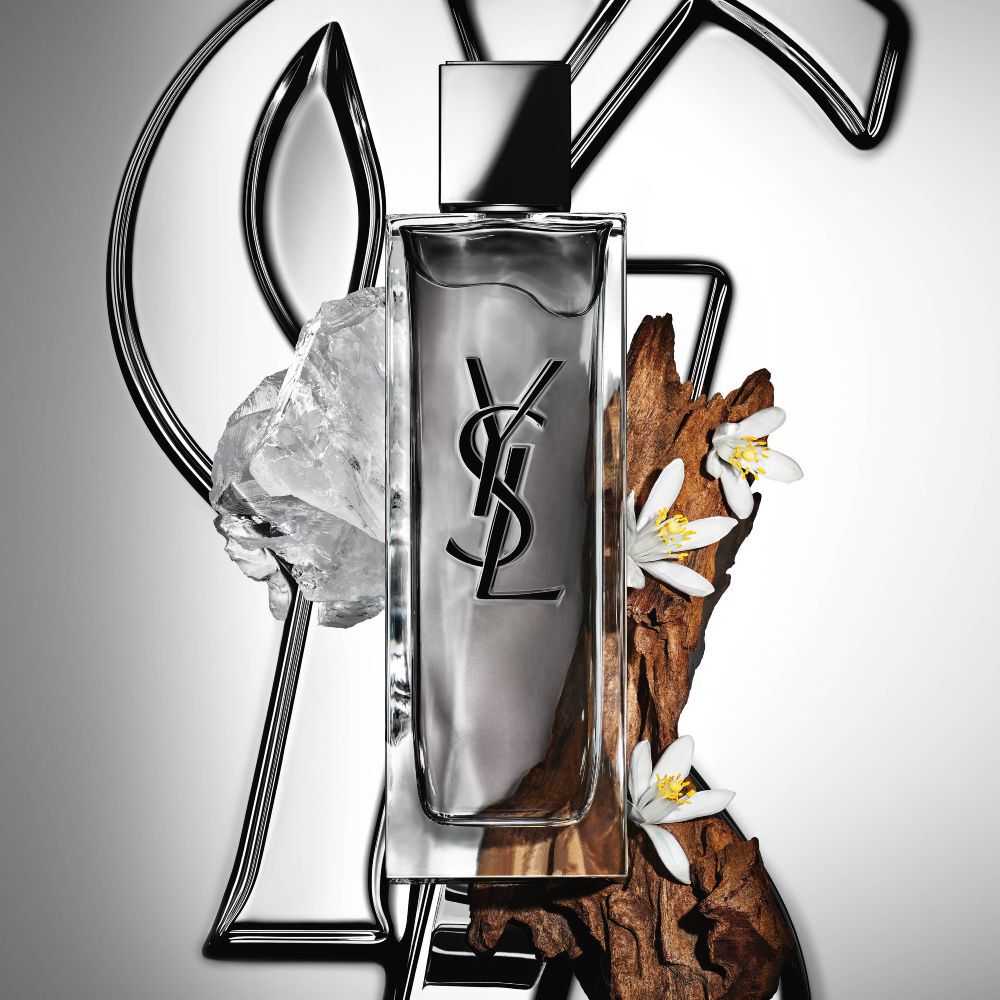 Vue en plongée de flacons de MYSLF Eau de Toilette Intense disposés sur de grandes lettres 3D noires formant le mot MYSLF, posées à plat sur le sol.