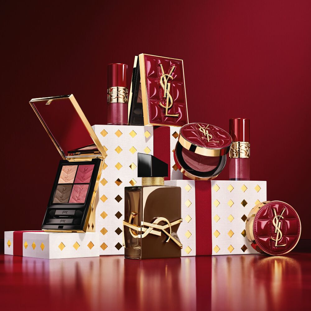 YSL Holiday 2026 makeup collection and fragrance set on gold-dotted white pedestals in burgundy.