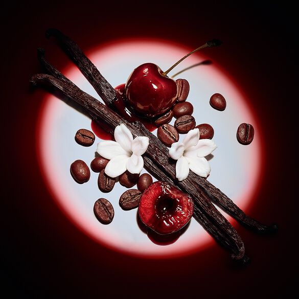 Gros plan sur des cerises rouges juteuses, des fleurs de jasmin, des gousses de vanille et des grains de café, révélés par un projecteur dramatique pour Black Opium Eau de Parfum Over Red.