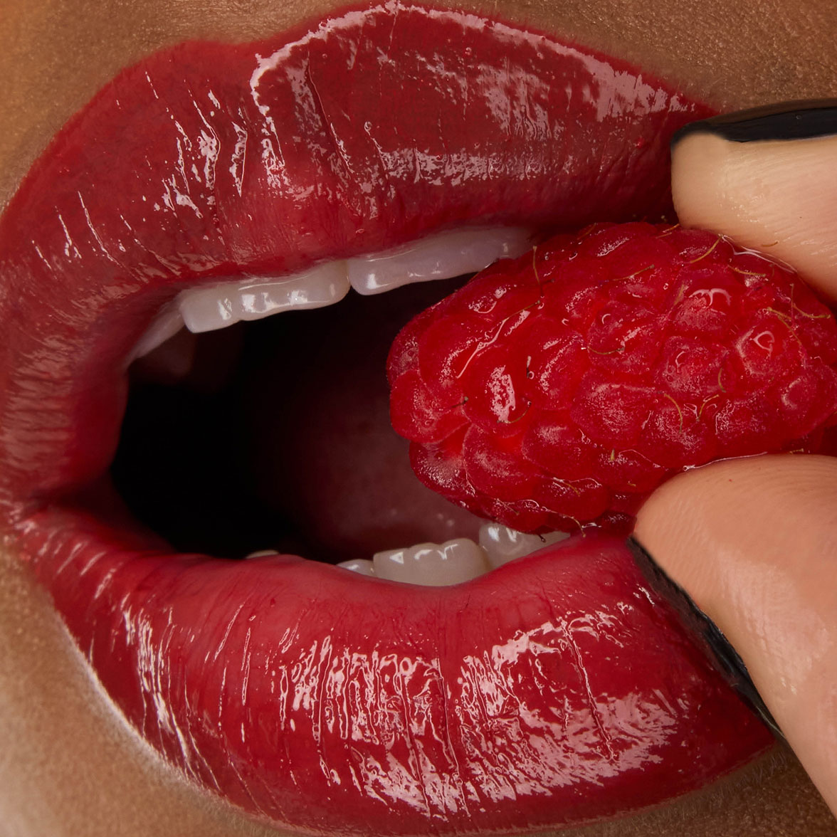 Close-up van de lippen van model Zahara, opgemaakt met YSL LOVESHINE Lipstick in de kleur Berry Crush (tint 219), terwijl ze een verse framboos vasthoudt.
