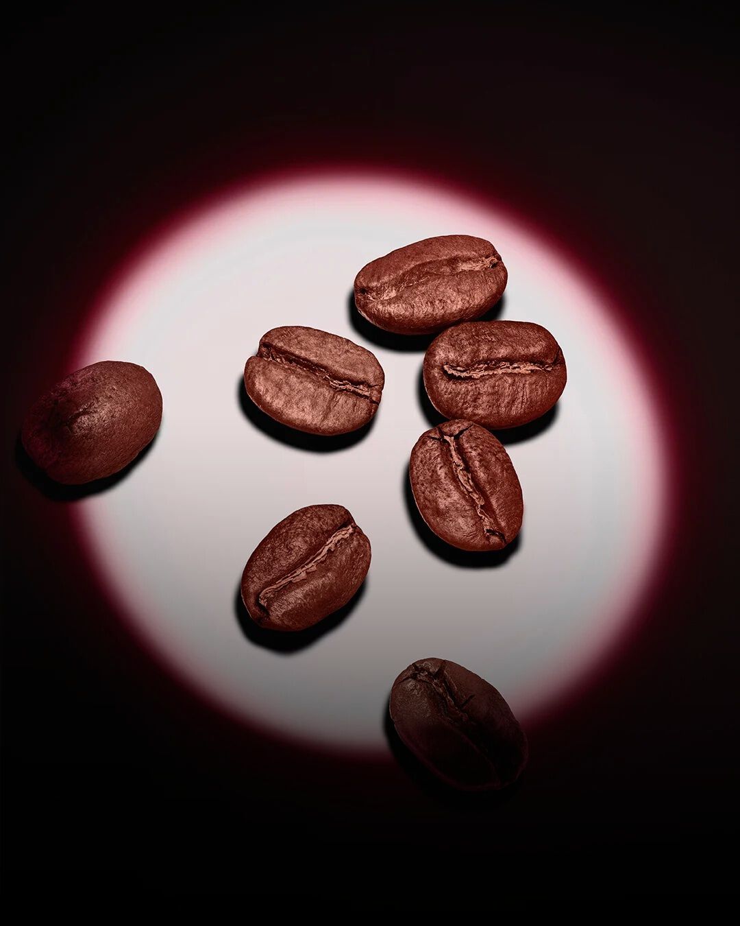 Een groep gebrande koffiebonen, uitgelicht door een roze ronde spot tegen een donkere achtergrond.