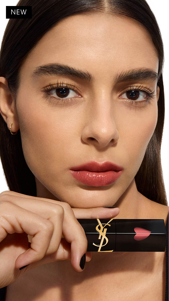Modèle à la peau mate, posant avec le YSL THE INKS VINYL CREAM tenu horizontalement sous son menton, affichant une teinte rose chaude et brillante.