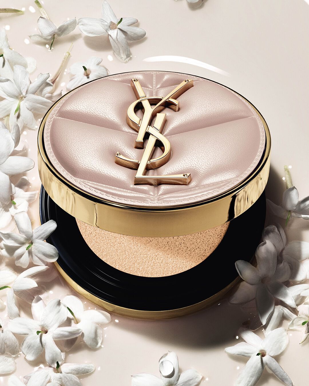 Gros plan du YSL SKIN AFFAIR SOFT GLOW CUSHION dans une flaque de fond de teint liquide et de fleurs de jasmin. Fini lumineux et sensoriel.