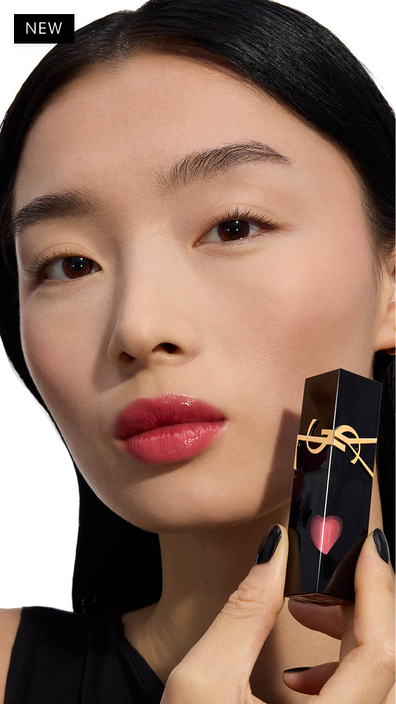 Modèle à la peau claire, lèvres brillantes dans une teinte rose-berry, tenant le flacon noir de YSL THE INKS VINYL CREAM avec son cœur rouge étincelant.
