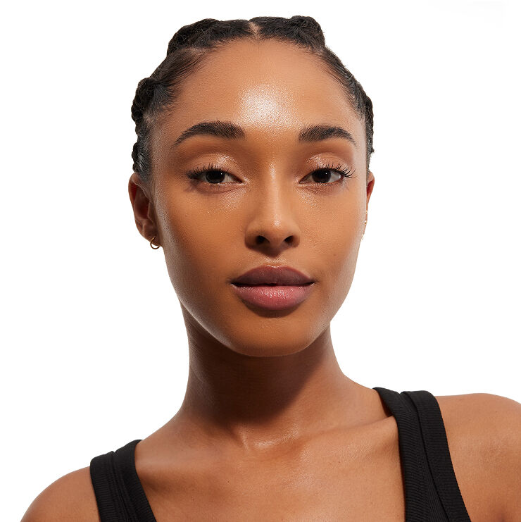 Portrait d'une femme aux cheveux tressés et à la peau impeccable, vêtue d'un haut noir, regardant directement le spectateur, mettant en valeur son maquillage.