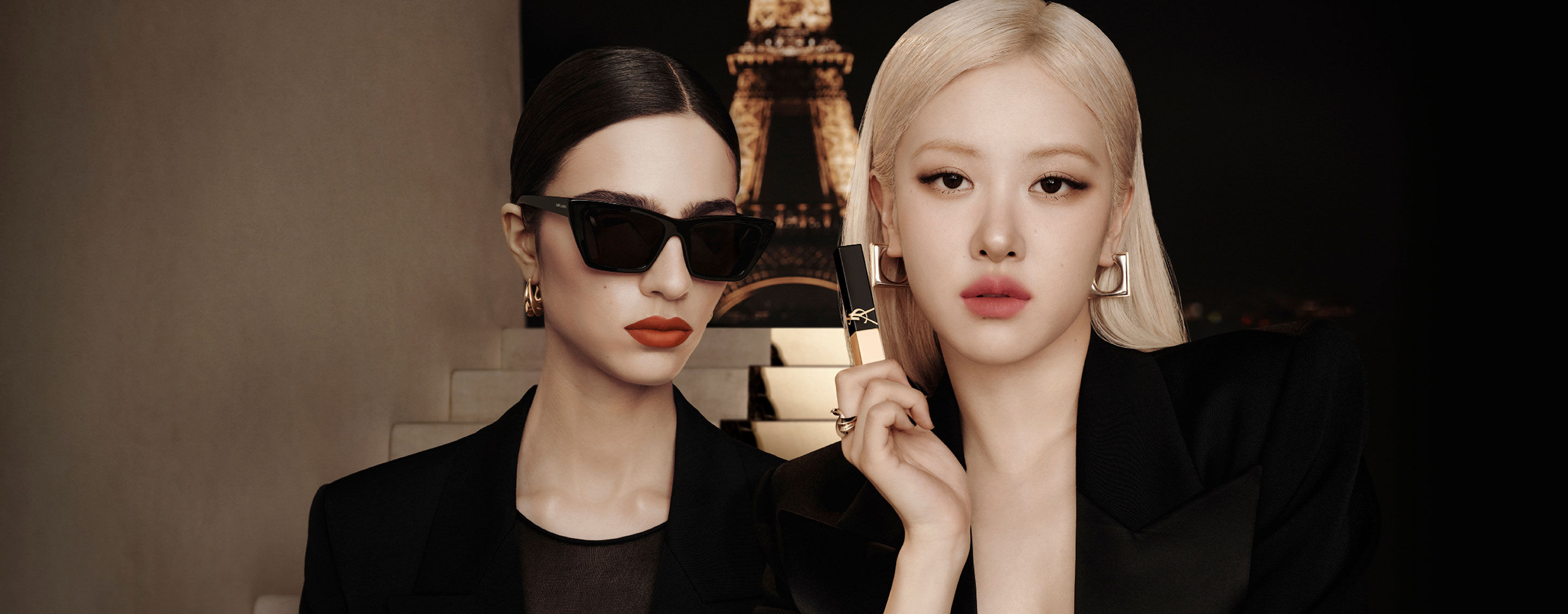 Deux mannequins en noir devant la tour Eiffel la nuit ; l’une tient un produit lèvres YSL noir‑or.