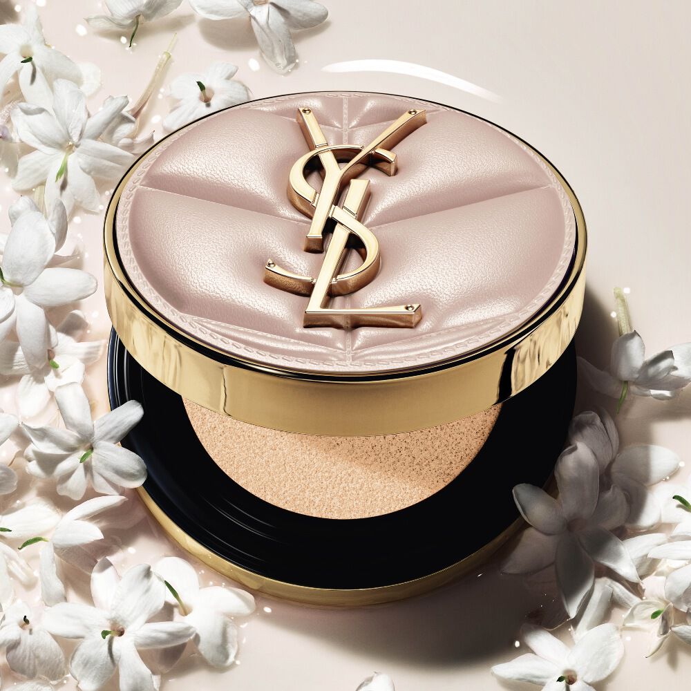 Gros plan du YSL SKIN AFFAIR SOFT GLOW CUSHION dans une flaque de fond de teint liquide et de fleurs de jasmin. Fini lumineux et sensoriel.