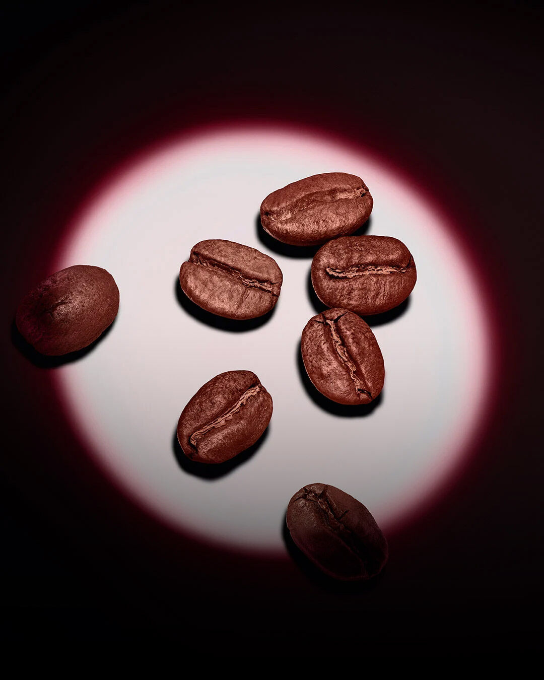 Een groep geroosterde koffiebonen verlicht door een roze cirkelvormige spotlight op een donkere achtergrond. 