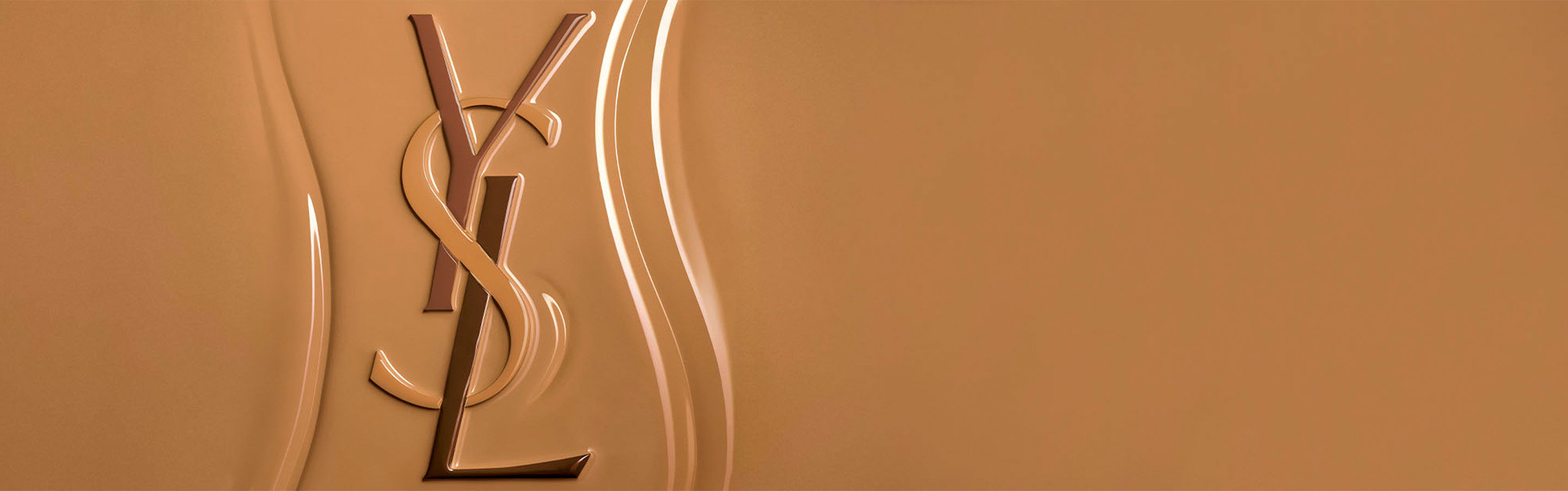 Logo Yves Saint Laurent (YSL) en relief sur une surface texturée de fond de teint liquide, soulignant la consistance riche et facile à estomper du produit.